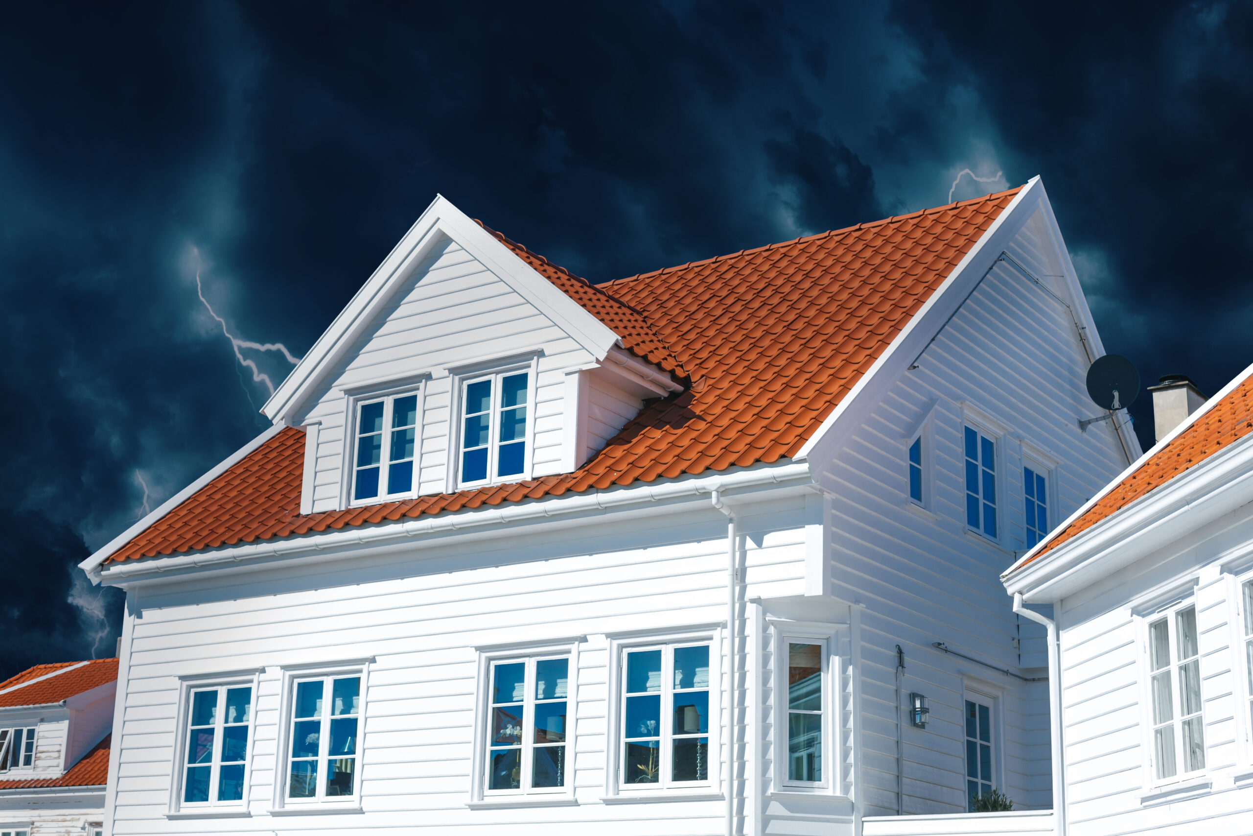 White wooden house with orange tiled roof against a dark stormy sky with lightning.